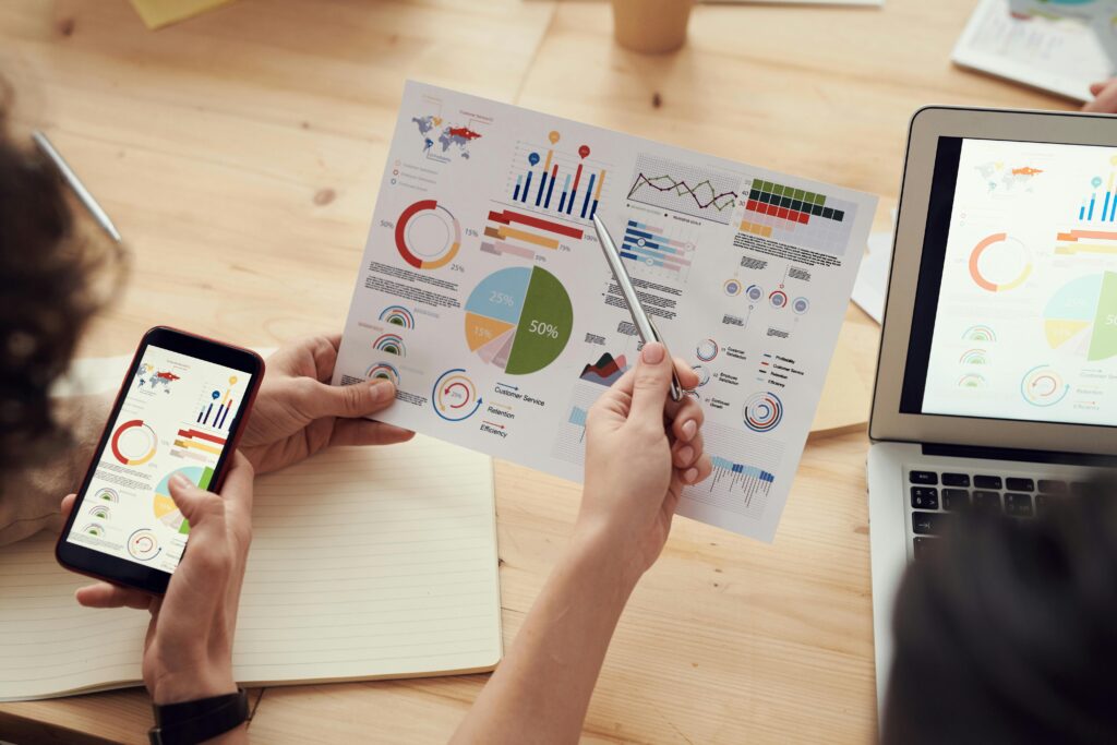 Team-Analyzing-Marketing-Report-With-Charts Hands reviewing a printed marketing report with colourful charts and graphs.